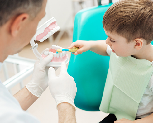 Little boy brushing model teeth held by dentist