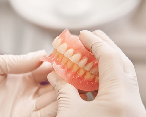 Gloved hands holding full dentures